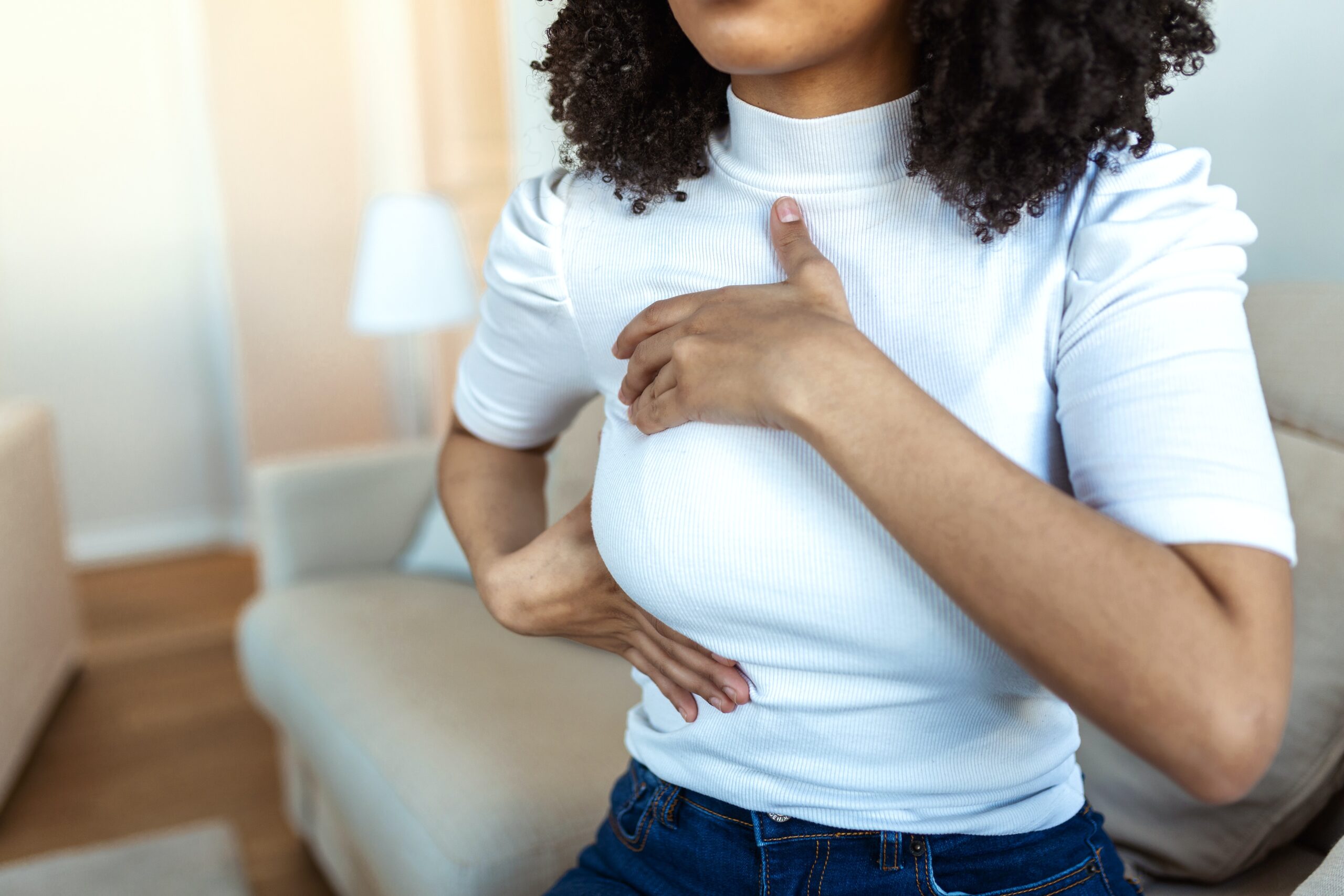 Young woman wearing white shirt self checking her breast for lumps
